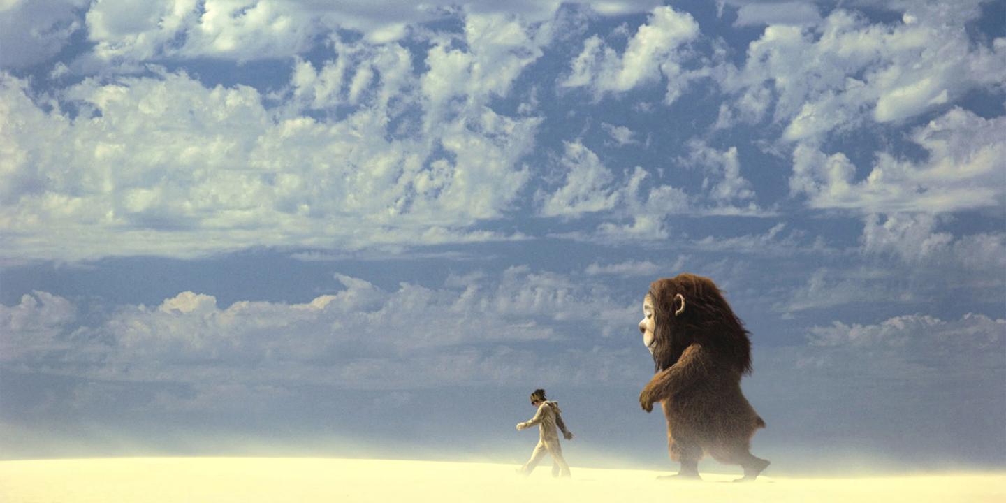 Still from the movie Where the Wild Things Are showing Max and a monster Carol walking across a sand desert under a bright blue sky.